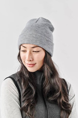 A grey Dockside Knit Beanie worn by a woman with long, wavy hair, paired with a dark vest.