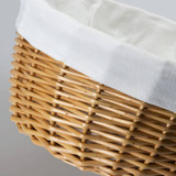 A wicker tote bag in natural bamboo tones with a cream-coloured fabric lining at the top and a textured weave pattern. A wicker tote bag in natural bamboo tones with a cream-coloured fabric lining at the top and a textured weave pattern.