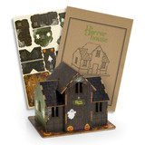 A wooden model of a spooky house in dark colours, accompanied by assembly sheets and a branded guide.