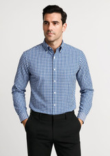 A blue and white checked long sleeve button-up shirt featuring a collar and a logo. The model stands with hands in pockets. A blue and white checked long sleeve button-up shirt featuring a collar and a logo. The model stands with hands in pockets.