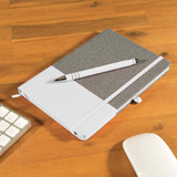 A grey and white notebook is shown with a matching pen resting on top, placed on a wooden desk alongside a keyboard and mouse. A grey and white notebook is shown with a matching pen resting on top, placed on a wooden desk alongside a keyboard and mouse.