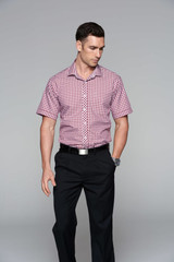A short sleeve button-up shirt in red and white checks, worn with dark trousers. The shirt has a branding logo.