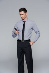 A long-sleeve button-up shirt in light grey, paired with black pants, worn by a man checking a phone. A long-sleeve button-up shirt in light grey, paired with black pants, worn by a man checking a phone.