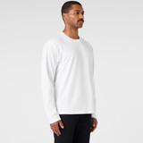 A white long-sleeve T-shirt is displayed on a model standing sideways, paired with black pants. The shirt has a logo.