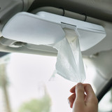 A white car sun visor tissue box with tissues being pulled out, mounted on a vehicle's interior.
