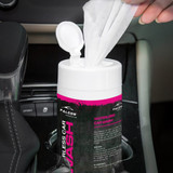 A white container with a flip-top lid holds wet tissues, featuring a bright pink label, placed in a car's cup holder.