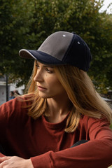A two-tone cap featuring contrasting stitching, with a grey body and darker peak, held by a person outdoors.