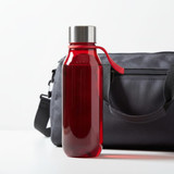 A drink bottle in vibrant red, featuring a stainless steel lid and a handle, beside a grey duffel bag.