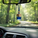 A car reed diffuser in blue glass with a wooden top, hanging from a rearview mirror amidst a forest backdrop.