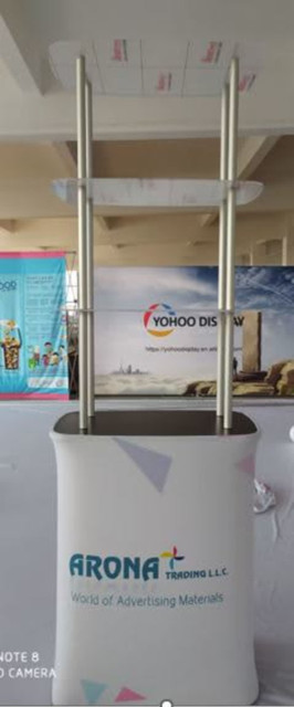 A promotional table featuring a stretch fabric design in white with metal shelves and a logo.