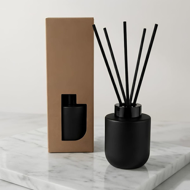 A black botanical reed diffuser with five reeds and a minimalist box on a marble surface.