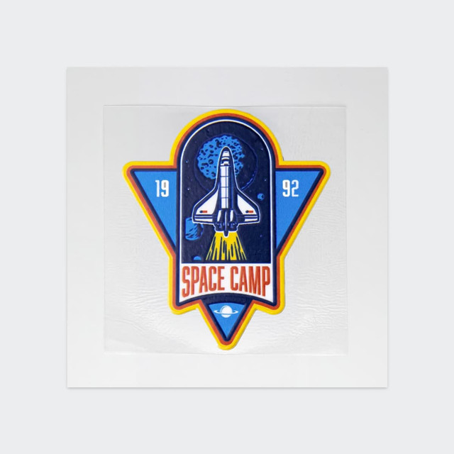 A blue and yellow sticker featuring a rocket and "Space Camp" text, set against a space-themed background.