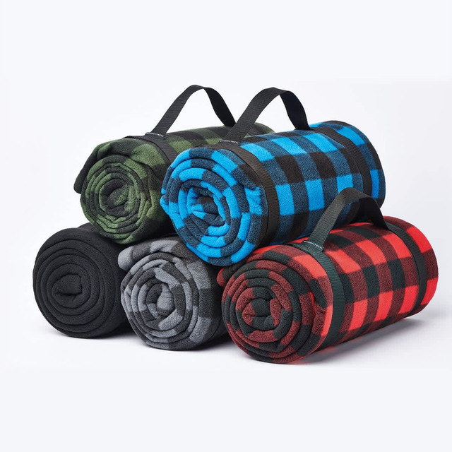 A stack of rolled fleece blankets in green, blue, grey, and red plaid patterns, each with a carrying handle. A stack of rolled fleece blankets in green, blue, grey, and red plaid patterns, each with a carrying handle.