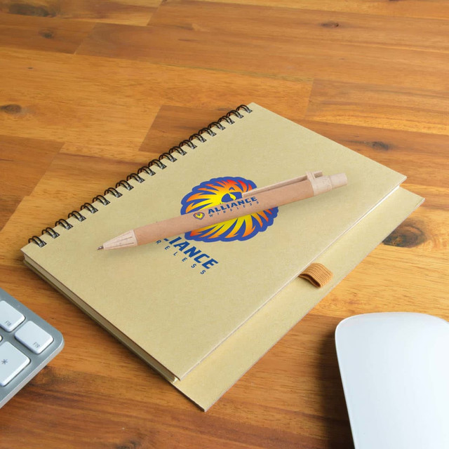 A brown spiral-bound notebook with a logo and a wooden pen resting on a wooden desk, next to a keyboard and mouse. A brown spiral-bound notebook with a logo and a wooden pen resting on a wooden desk, next to a keyboard and mouse.