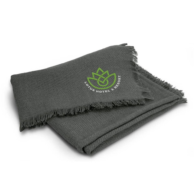 A dark green throw blanket with a textured pattern and a logo in the corner. The edges are fringed. A dark green throw blanket with a textured pattern and a logo in the corner. The edges are fringed.