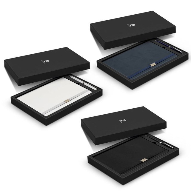 A gift set featuring a navy, white, and black notebook, each with a matching pen, in sleek black packaging. A gift set featuring a navy, white, and black notebook, each with a matching pen, in sleek black packaging.