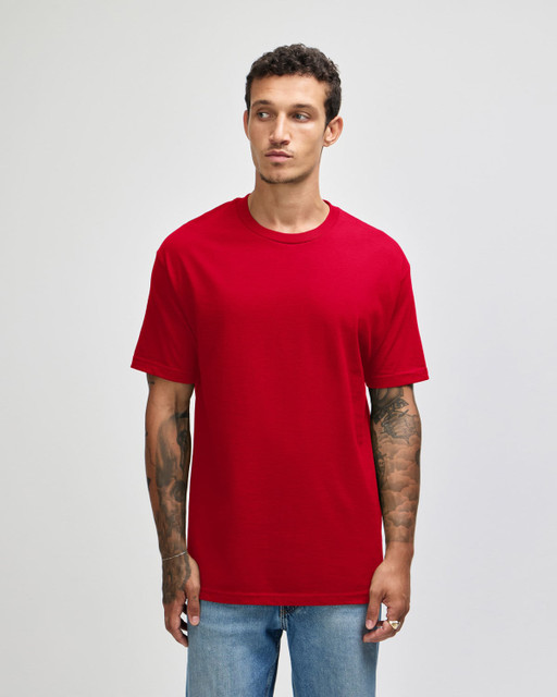 A red unisex t-shirt made from heavyweight cotton, featuring a classic fit. The model has tattoos and is wearing blue jeans.