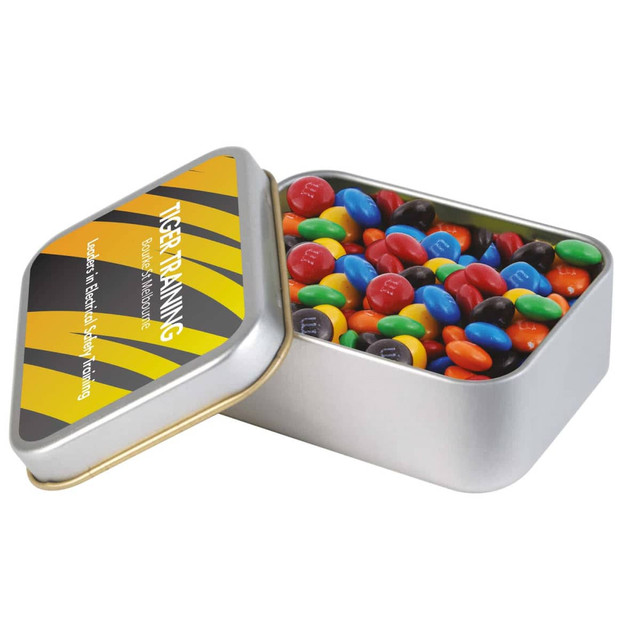 A silver rectangular tin filled with colourful M&M's chocolate candies. The tin has a logo. A silver rectangular tin filled with colourful M&M's chocolate candies. The tin has a logo.