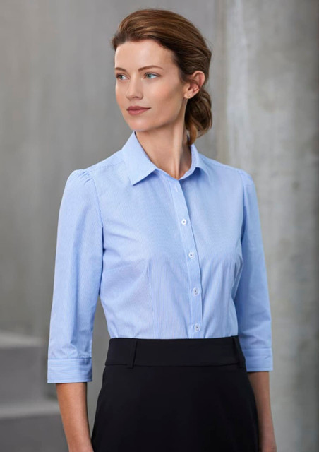A women's button-up shirt in light blue, featuring 3/4 sleeves, with a collar and a fitted design. It has a logo.
