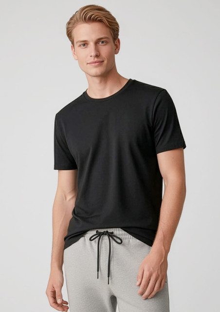 A black short sleeve tee worn by a model, paired with grey pants. The shirt features a logo.