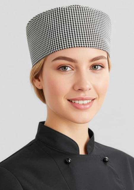 A chef cap in a black and white checkered pattern worn by a smiling individual in a black chef uniform.