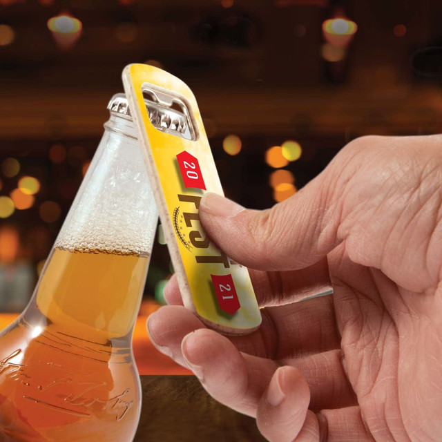 A drink bottle opener in yellow and silver being used to open a glass bottle with beer. The image includes a logo. A drink bottle opener in yellow and silver being used to open a glass bottle with beer. The image includes a logo.