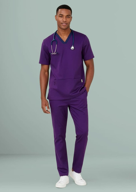 A man in a purple scrub top and matching straight leg scrub pants, wearing a stethoscope around his neck.