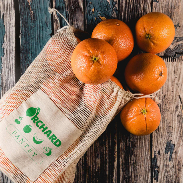 A mesh produce bag in natural colour, filled with bright orange oranges, displayed on a rustic wooden surface. A mesh produce bag in natural colour, filled with bright orange oranges, displayed on a rustic wooden surface.
