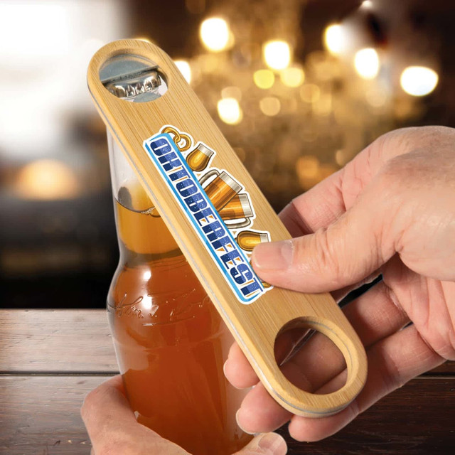 A drink bottle opener made of bamboo, featuring a logo, held over a bottle against a blurred background. A drink bottle opener made of bamboo, featuring a logo, held over a bottle against a blurred background.