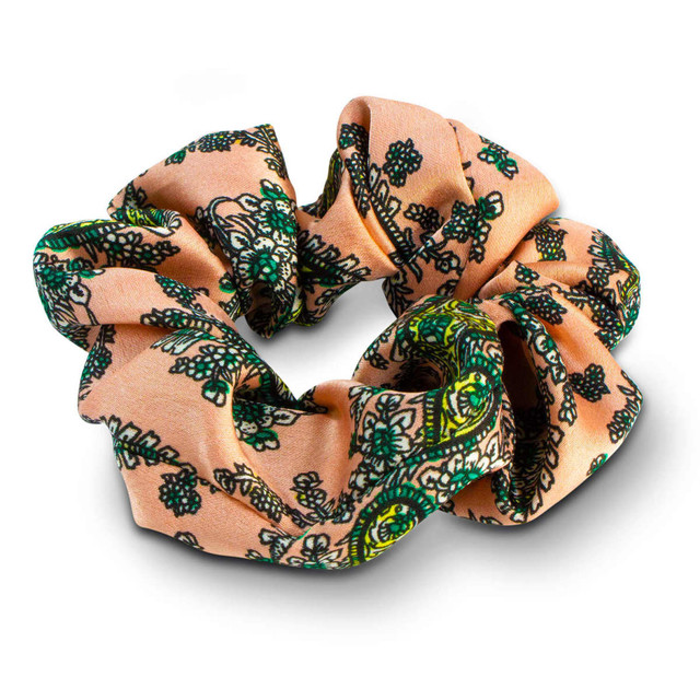 A fabric hair scrunchie in peach with green floral patterns, featuring a decorative design. A fabric hair scrunchie in peach with green floral patterns, featuring a decorative design.