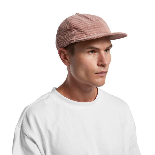 A cord cap in a soft pink hue displayed on a model wearing a white shirt. Features a flat brim and logo.