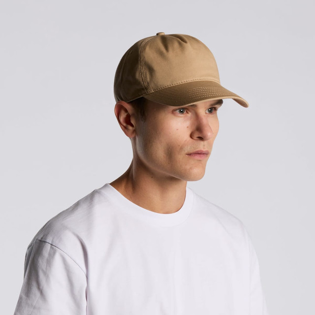 A tan soft cap with a structured design, worn by a model in a plain white t-shirt. It features a logo on the front. A tan soft cap with a structured design, worn by a model in a plain white t-shirt. It features a logo on the front.