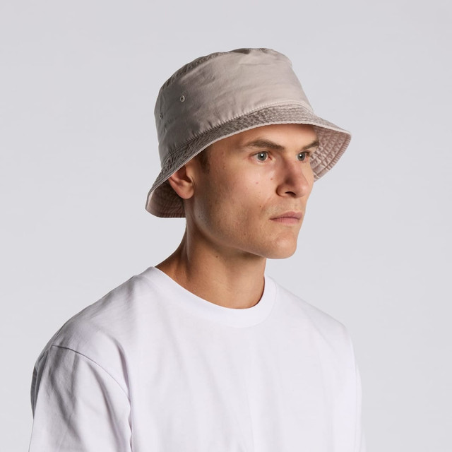 A beige bucket hat worn by a model, featuring stitching details and a visible brand logo. A beige bucket hat worn by a model, featuring stitching details and a visible brand logo.