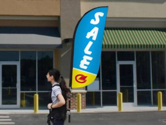 A small single-sided backpack wing banner in blue and yellow, attached to a person walking near a store.