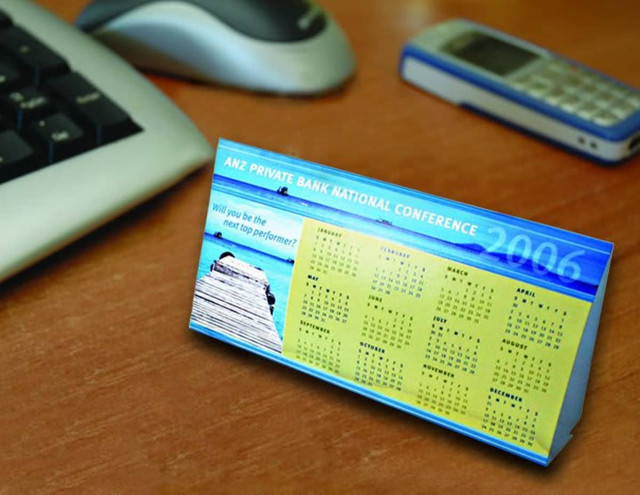 A budget desk calendar with a blue and yellow design, featuring a yearly calendar layout and a scenic image. A budget desk calendar with a blue and yellow design, featuring a yearly calendar layout and a scenic image.