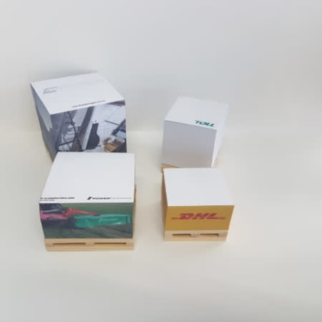 A set of cube notepads in various sizes, featuring colourful designs and logos, displayed on small wooden pallets. A set of cube notepads in various sizes, featuring colourful designs and logos, displayed on small wooden pallets.
