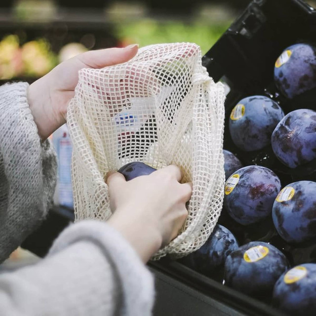 A mesh produce bag in natural colour, being used to hold plums in a grocery store.