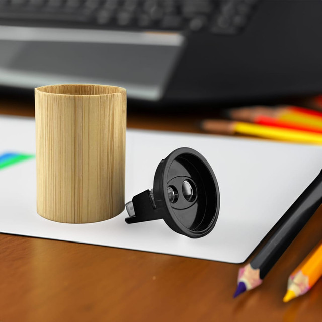 A bamboo pencil sharpener with a black mechanism, placed on a desk near coloured pencils and a notepad.
