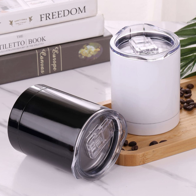 A drinkware set featuring a black and a white mug, both with clear lids, on a marble surface with coffee beans.