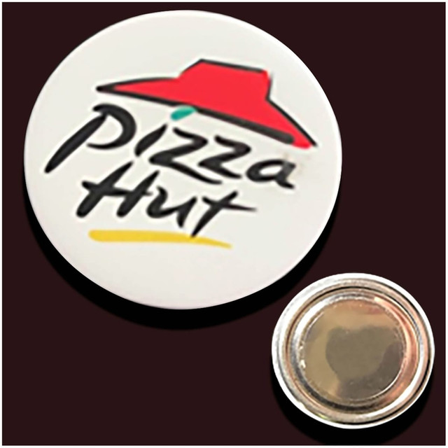A white button badge featuring a red hat design and a logo, with a shiny silver backing. A white button badge featuring a red hat design and a logo, with a shiny silver backing.