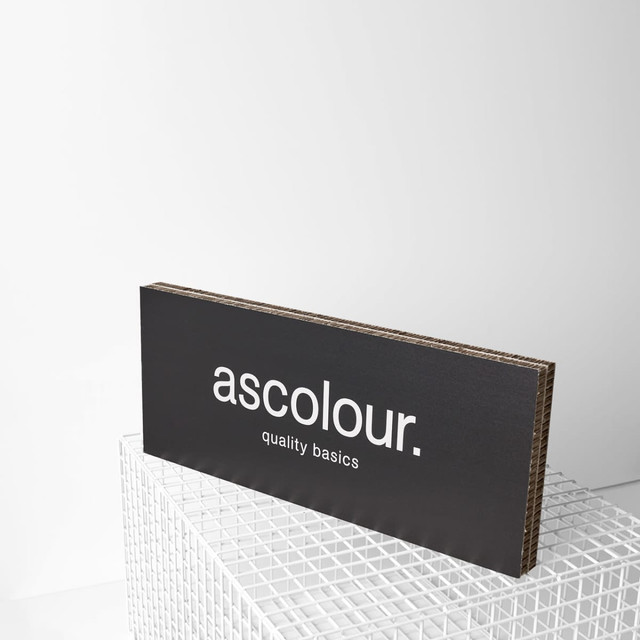 A black branded plaque with a logo displayed on a white grid surface. The plaque features a simple, modern design. A black branded plaque with a logo displayed on a white grid surface. The plaque features a simple, modern design.