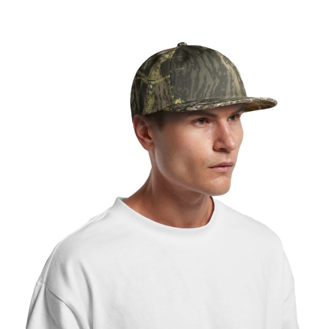 A camo cap in shades of green and brown, featuring a flat brim and a structured design, worn by a model.