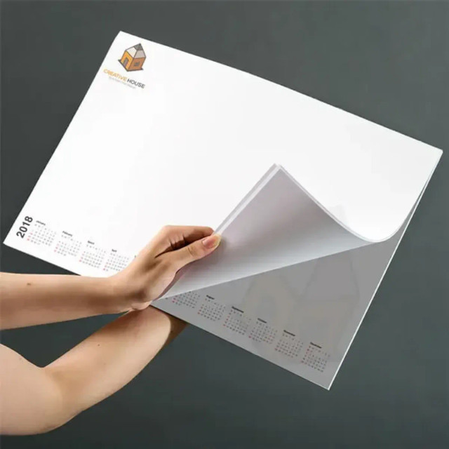 A desk pad with a white design, featuring numerous calendar pages and a logo in the top corner. A desk pad with a white design, featuring numerous calendar pages and a logo in the top corner.