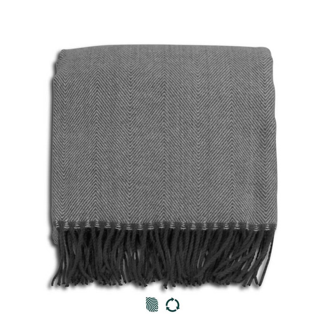 A grey herringbone throw blanket with fringed edges, neatly folded. It features a logo in one corner.