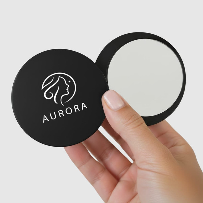 A compact mirror held in a hand, featuring a black case with a logo on one side and a reflective surface.