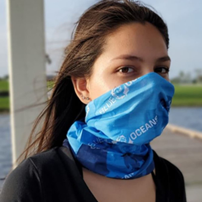 A blue Coolmax bandana wrapped around a person's neck, featuring a logo, in an outdoor setting near water.