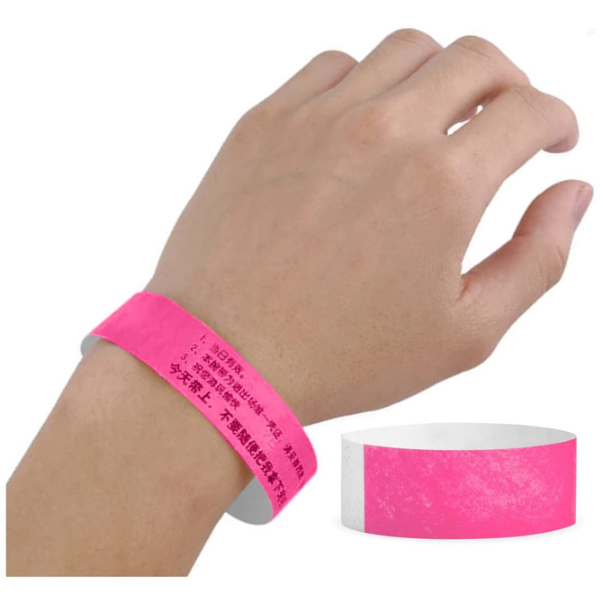 A pink Tyvek wristband is worn on a hand, with a smooth white interior. The wristband features some printed details and a logo.