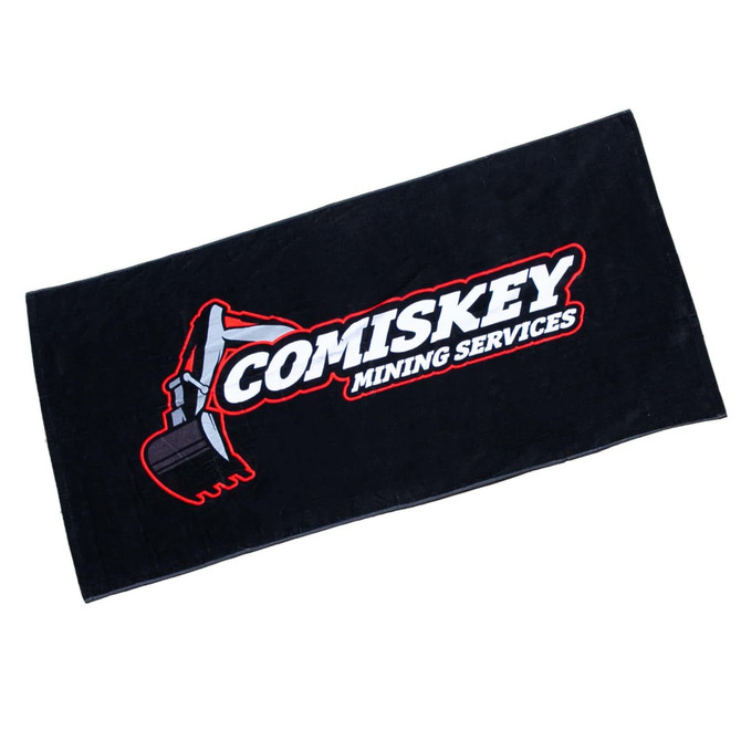 A black beach towel measuring 75cm x 150cm, featuring a logo and design related to Comiskey Mining Services.