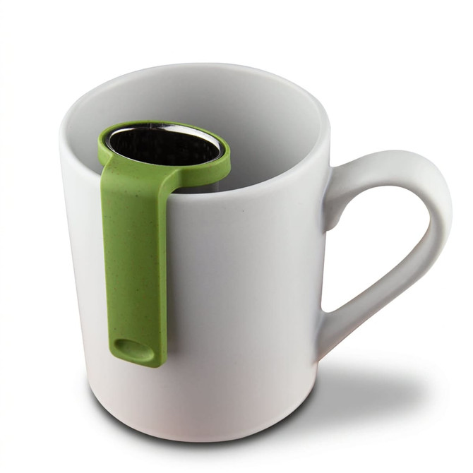 A white mug with a green travel tea infuser resting on the rim. The infuser is metallic with a mesh design.