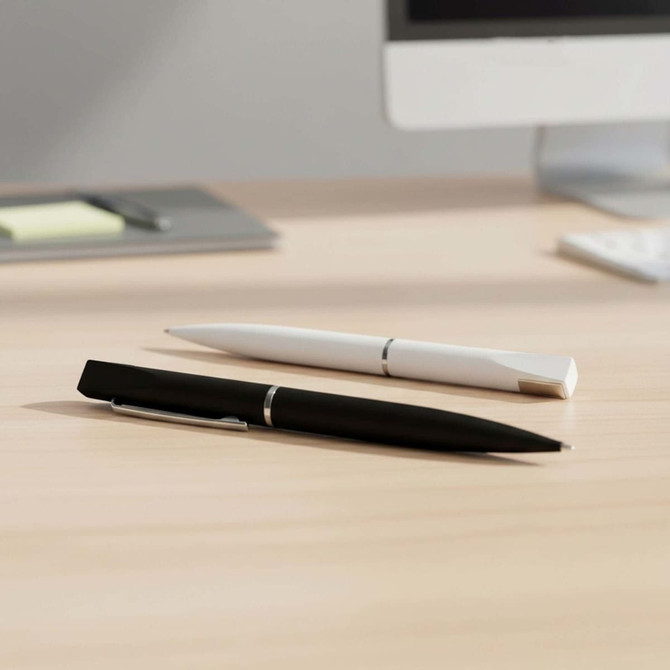 A black and a white pen rest on a wooden desk beside a computer, showcasing a sleek design and metallic accents.
